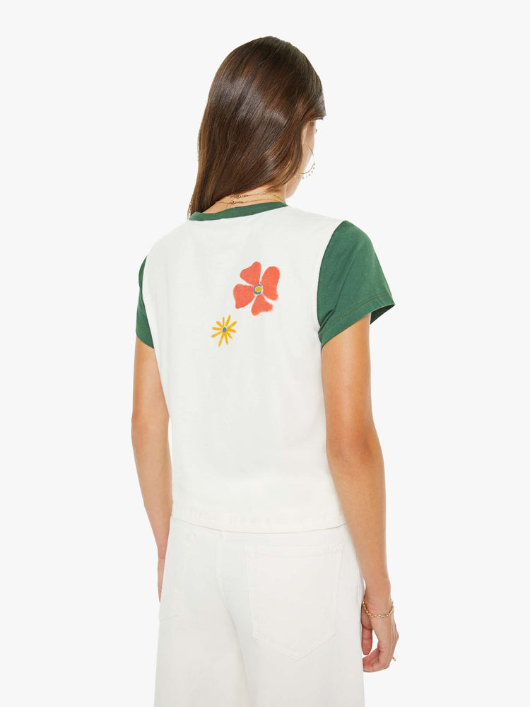 Back view of a woman in off-white with green trim tee features blue block text and a smiley face graphic on the front.