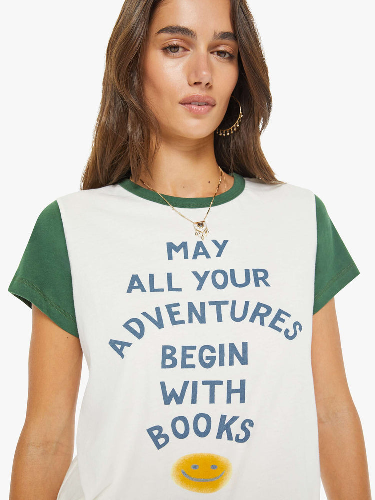 Close up view of a woman in off-white with green trim tee features blue block text and a smiley face graphic on the front.