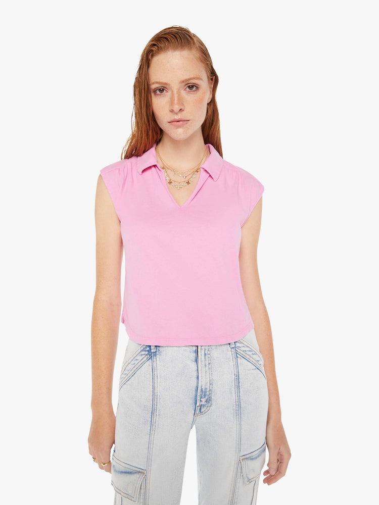 A front view of a woman wearing a pink polo collar tee featuring cap sleeves and a cropped curve hem, paired with a pair of light blue acid wash jeans.