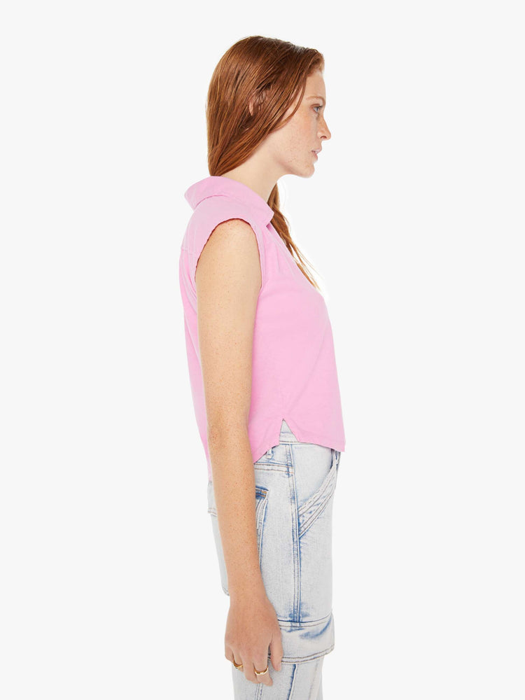 A side view of a woman wearing a pink polo collar tee featuring cap sleeves and a cropped curve hem, paired with a pair of light blue acid wash jeans.