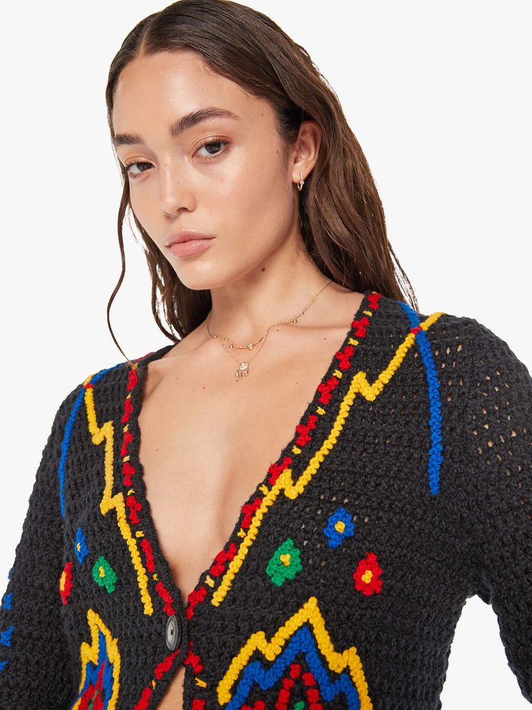 Close up view of a woman in a black with colorful flowers, shapes and trim knit top with a deep V-neck, extra long sleeves and a single button closure.