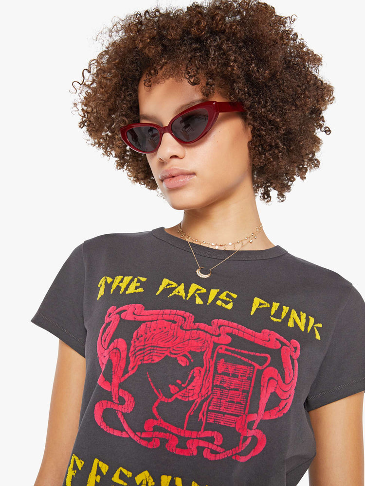 Close up view of a woman in a faded black tee features a yellow and red text graphic inspired by a punk music festival.