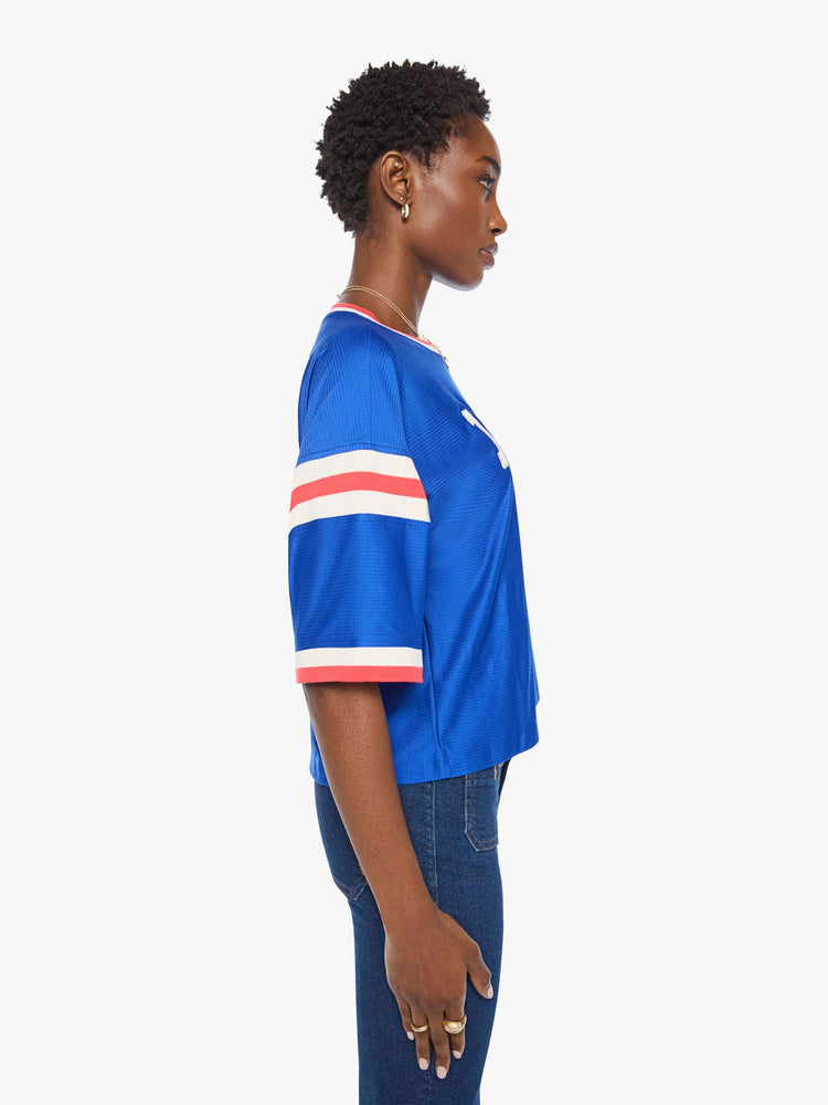 Side view of a woman in top is made from bright blue mesh with red and white striped details on the neck and sleeves and MOTHER's name in white across the chest.