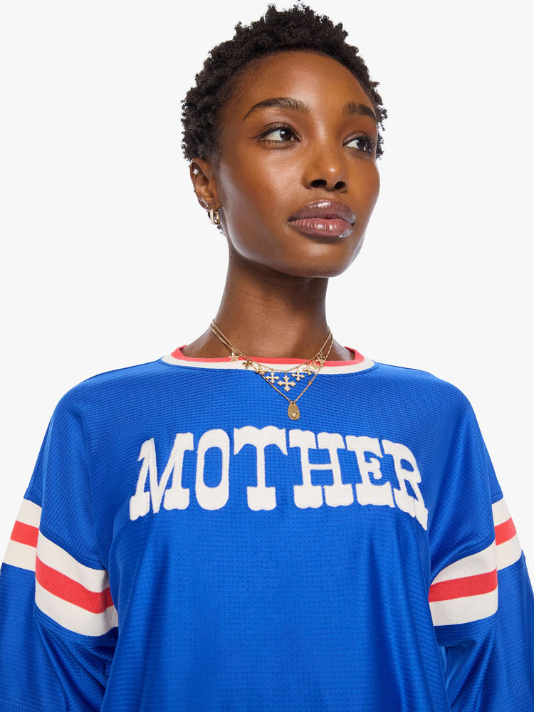 Close up view of a woman in top is made from bright blue mesh with red and white striped details on the neck and sleeves and MOTHER's name in white across the chest.