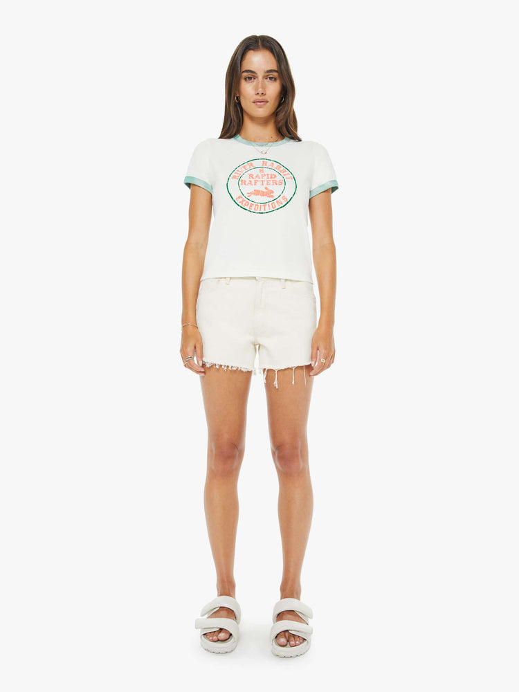 Full body view of a woman in a white with green trim tee with a flocked graphic on the front inspired by a rafting expedition logo.