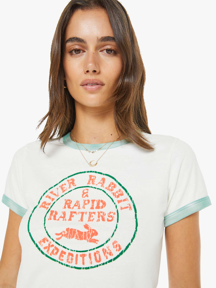 Close up view of a woman in a white with green trim tee with a flocked graphic on the front inspired by a rafting expedition logo.