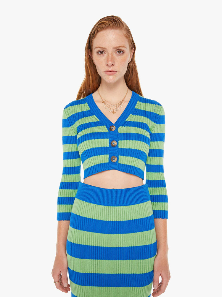 A front view of a woman wearing a green and blue striped cardigan featuring three brown buttons and a cropped body.