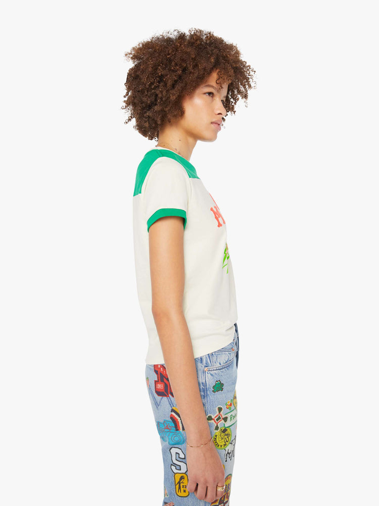 Side view of a woman in an off-white with green details tee and features a hand-drawn motorcycle graphic and MOTHER's name in pink fuzzy text on the chest.