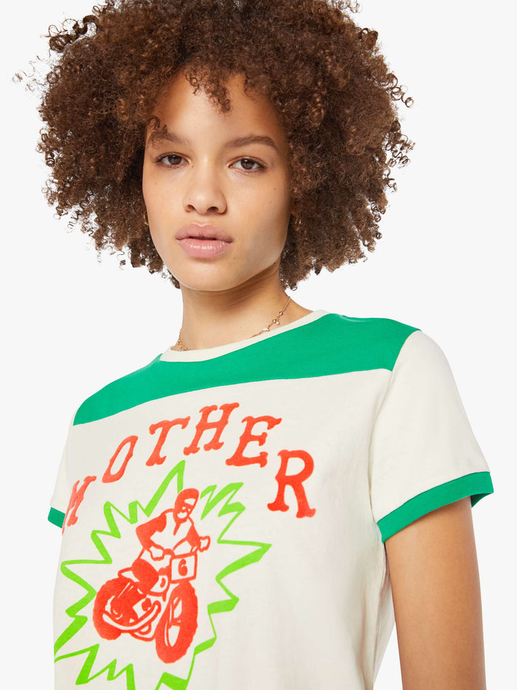 Close up view of a woman in an off-white with green details tee and features a hand-drawn motorcycle graphic and MOTHER's name in pink fuzzy text on the chest.