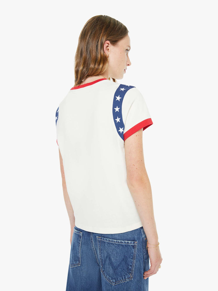 Back view of a woman in an off-white, the tee with white stars along the sleeves, red trim and MOTHER's name in green across the front — finished with a raised, velvety flocked texture.
