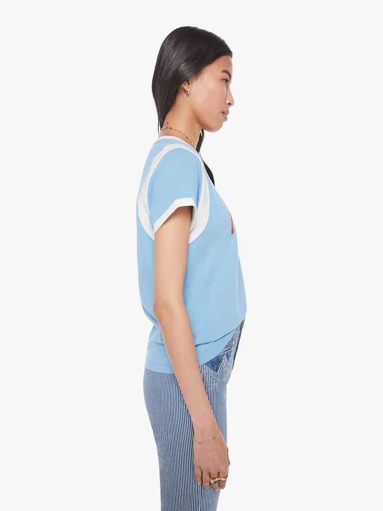 Side view of a woman in a baby blue with white trim and red cursive  patch in the front tee with extra-short sleeves, inset details at the shoulders and a loose, boxy fit. 