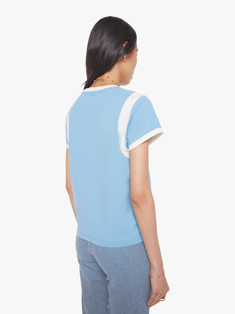 Back view of a woman in a baby blue with white trim and red cursive  patch in the front tee with extra-short sleeves, inset details at the shoulders and a loose, boxy fit. 