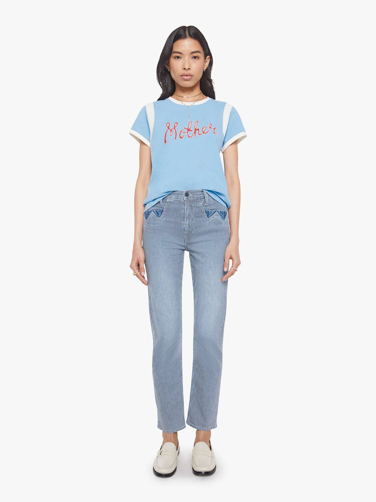 Full body view of a woman in a baby blue with white trim and red cursive  patch in the front tee with extra-short sleeves, inset details at the shoulders and a loose, boxy fit. 