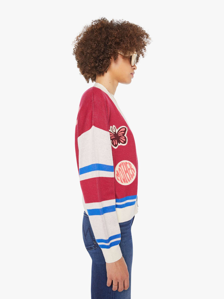 Side view of a woman in a faded red with athletic-inspired stripes across the sleeves  V-neck cardigan with drop shoulders.