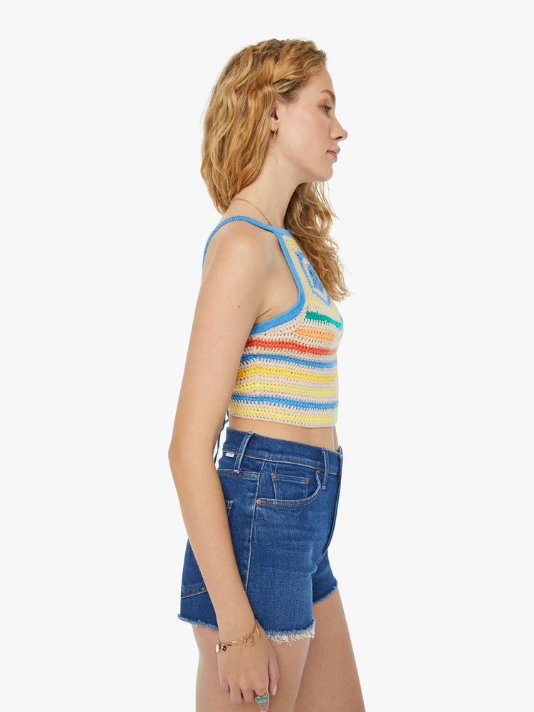 Side view of a woman in cream and rainbow striped crochet tank top that has narrow straps, a scoop neck and a cinch in the back that ties with openwork details and a flower motif at the chest.