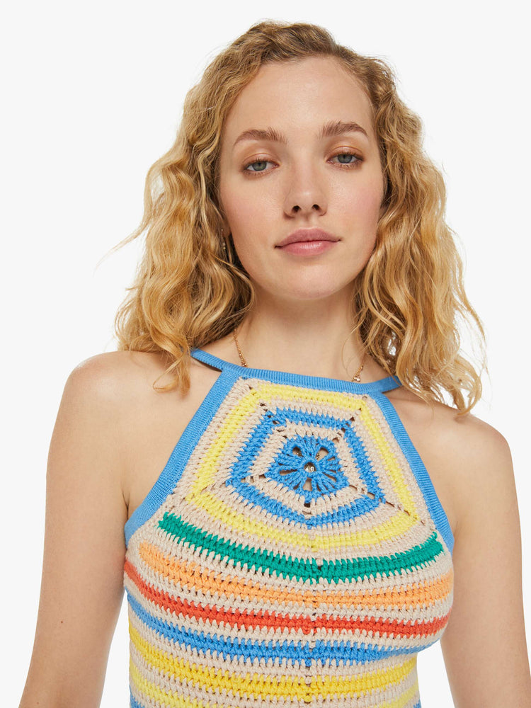 Detailed view of a woman in cream and rainbow striped crochet tank top that has narrow straps, a scoop neck and a cinch in the back that ties with openwork details and a flower motif at the chest.
