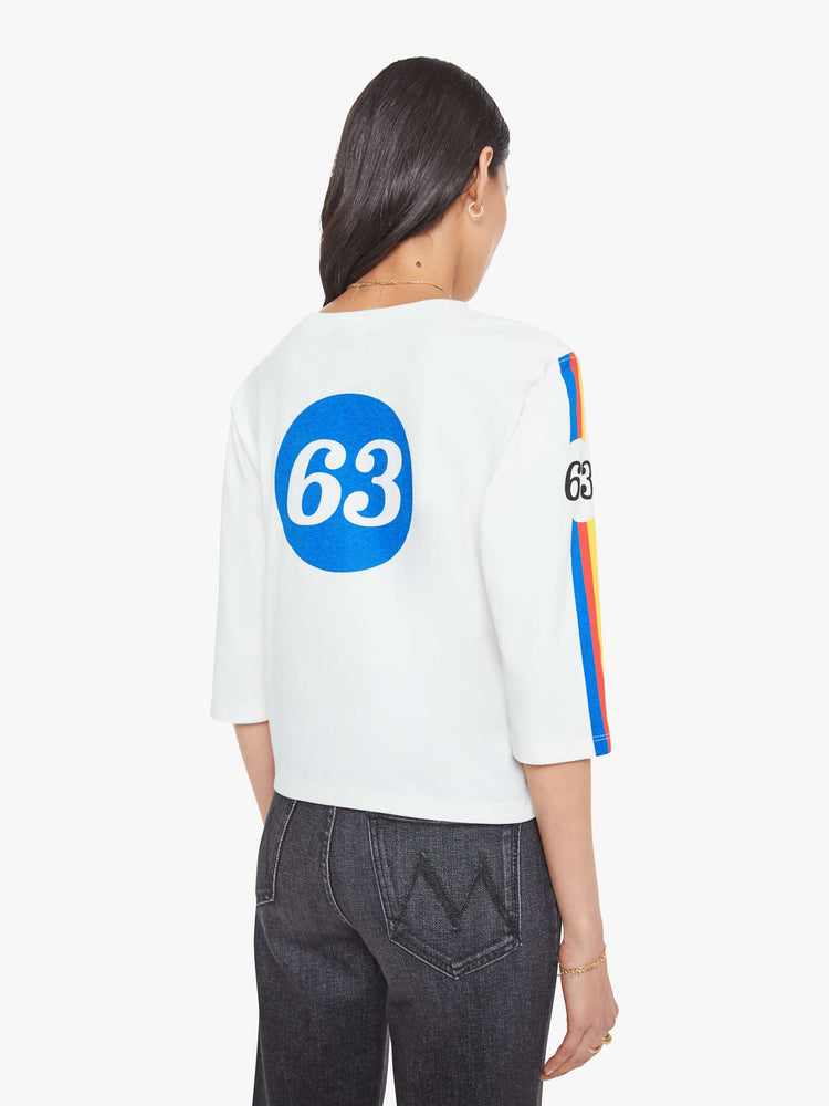Back view of a woman in crewneck tee with elbow-length sleeves and a loose, boxy fit in a white tee with a colorful stripes across the chest.