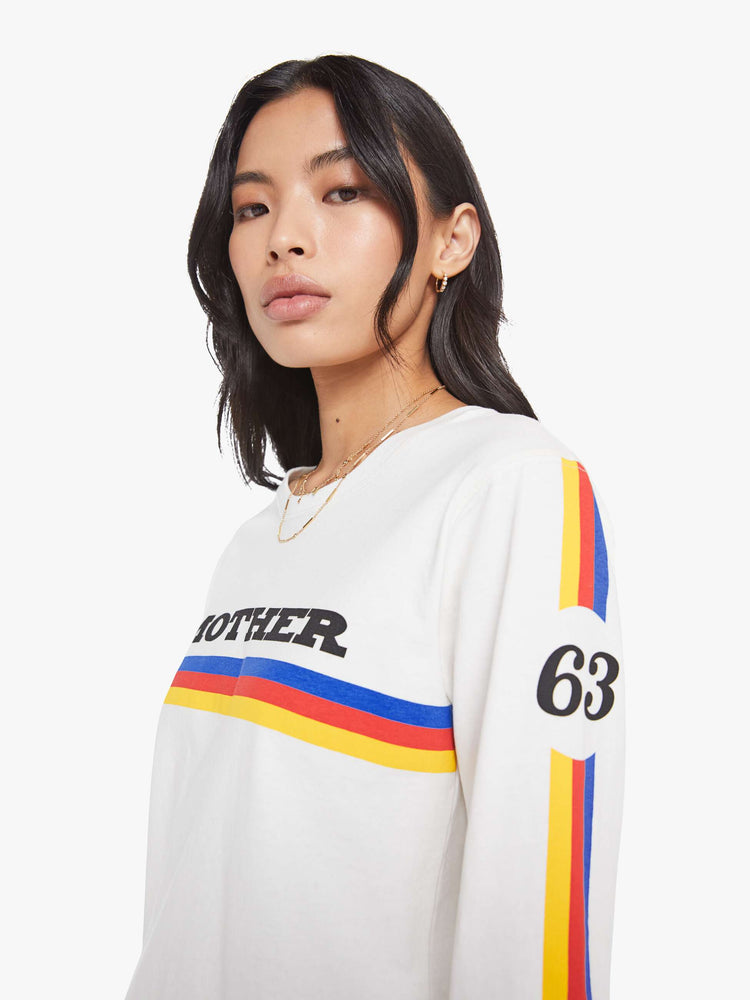 Close up view of a woman in crewneck tee with elbow-length sleeves and a loose, boxy fit in a white tee with a colorful stripes across the chest.