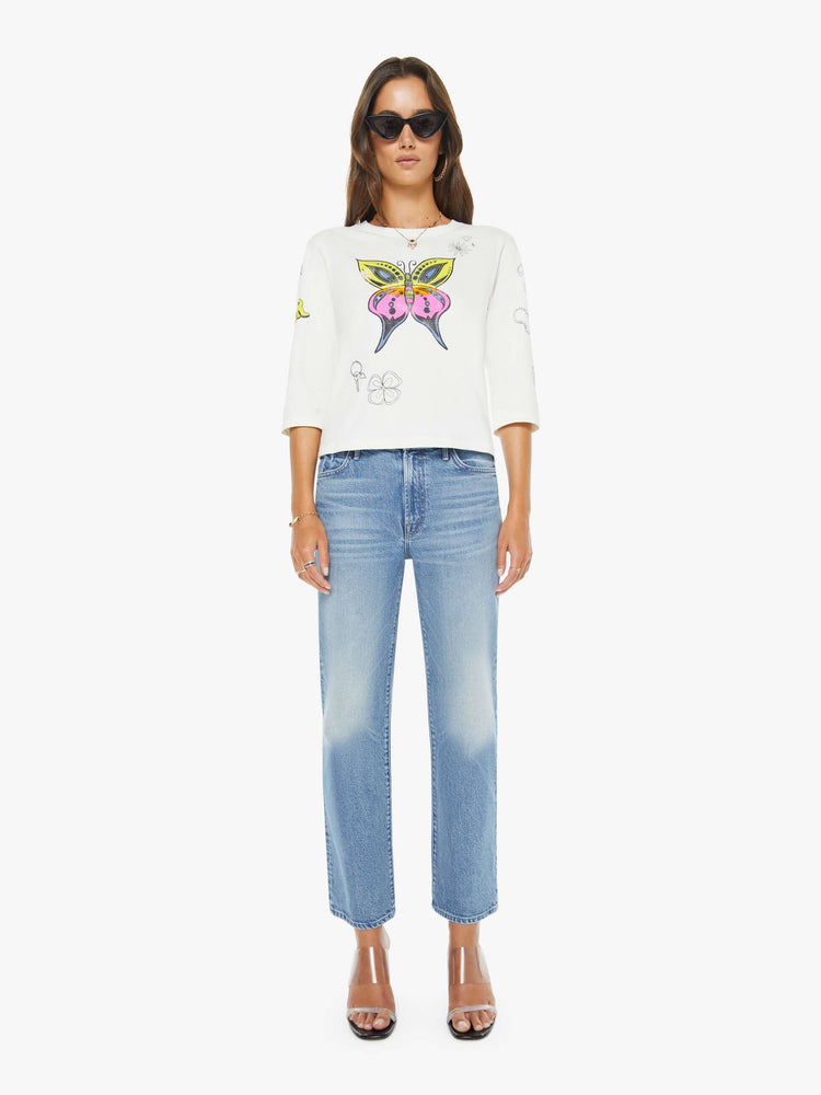 Full body view of a woman in a white with colorful butterfly crewneck tee with elbow-length sleeves and a loose, boxy fit.