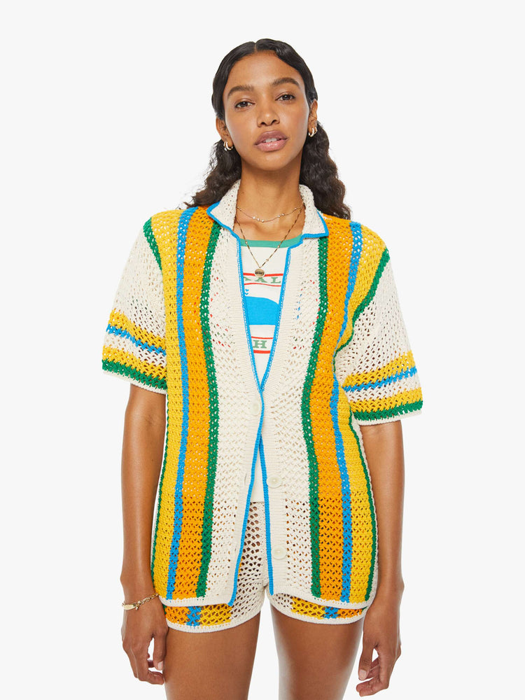 Front view of a woman in a cream, orange, green and blue striped crochet shir twith drop shoulders and a loose, oversized fit featuring delicate openwork details.