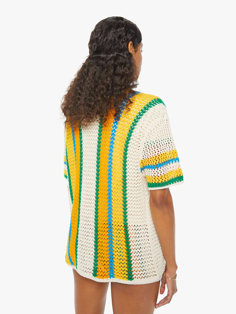 Back view of a woman in a cream, orange, green and blue striped crochet shir twith drop shoulders and a loose, oversized fit featuring delicate openwork details.