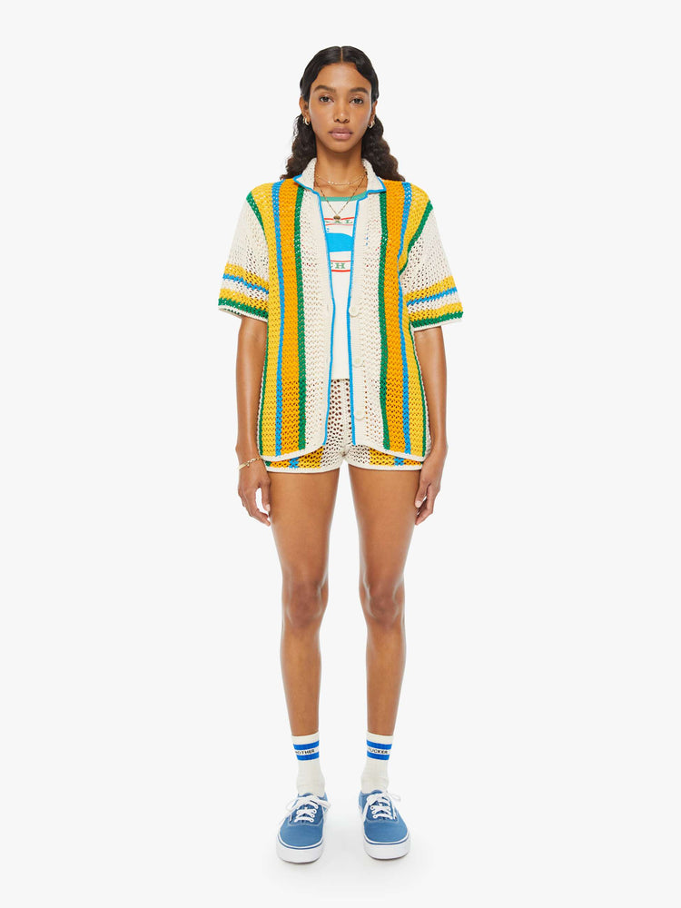 Full front view of a woman in a cream, orange, green and blue striped crochet shir twith drop shoulders and a loose, oversized fit featuring delicate openwork details.