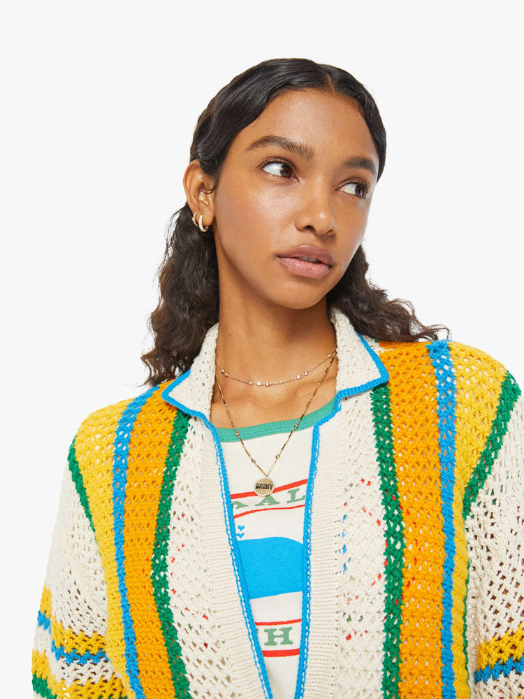 Detailed view of a woman in a cream, orange, green and blue striped crochet shir twith drop shoulders and a loose, oversized fit featuring delicate openwork details.