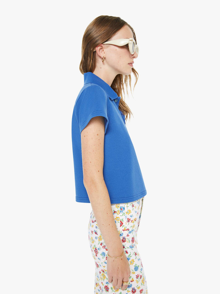 Side view of a woman in a blue cropped polo shirt with a two-button placket, short sleeves and a cropped fit.