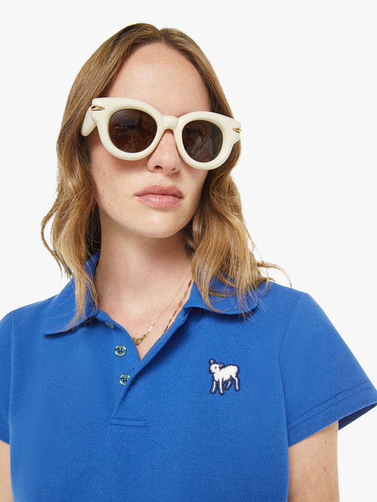 Close up view of a woman in a blue cropped polo shirt with a two-button placket, short sleeves and a cropped fit.