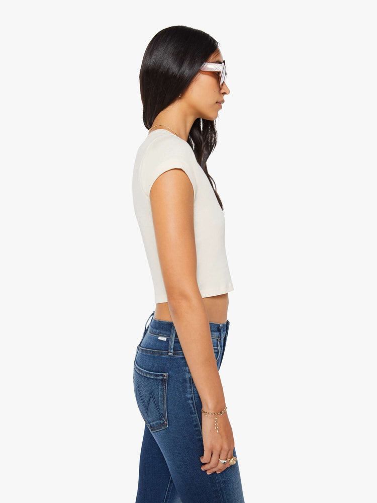 Side view of a woman in an off white crewneck tee with extra-short sleeves and a narrow fit.