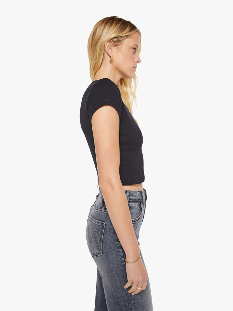 Side view of a woman in a black shrunken crewneck tee with extra-short sleeves and a cropped length.