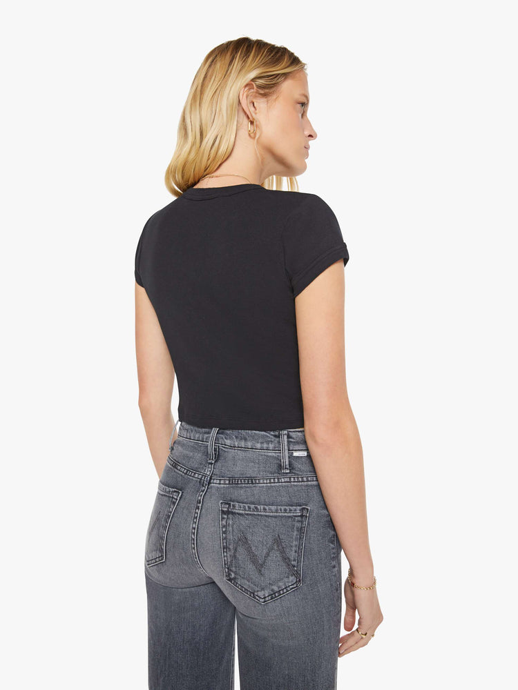 Back view of a woman in a black shrunken crewneck tee with extra-short sleeves and a cropped length.