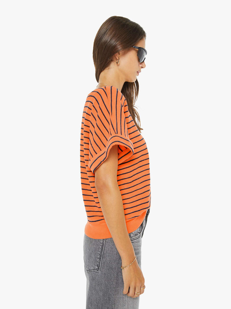 Side view of a woman in a bright orange and black stripes short sleeve tee with a boat neck and boxy fit.
