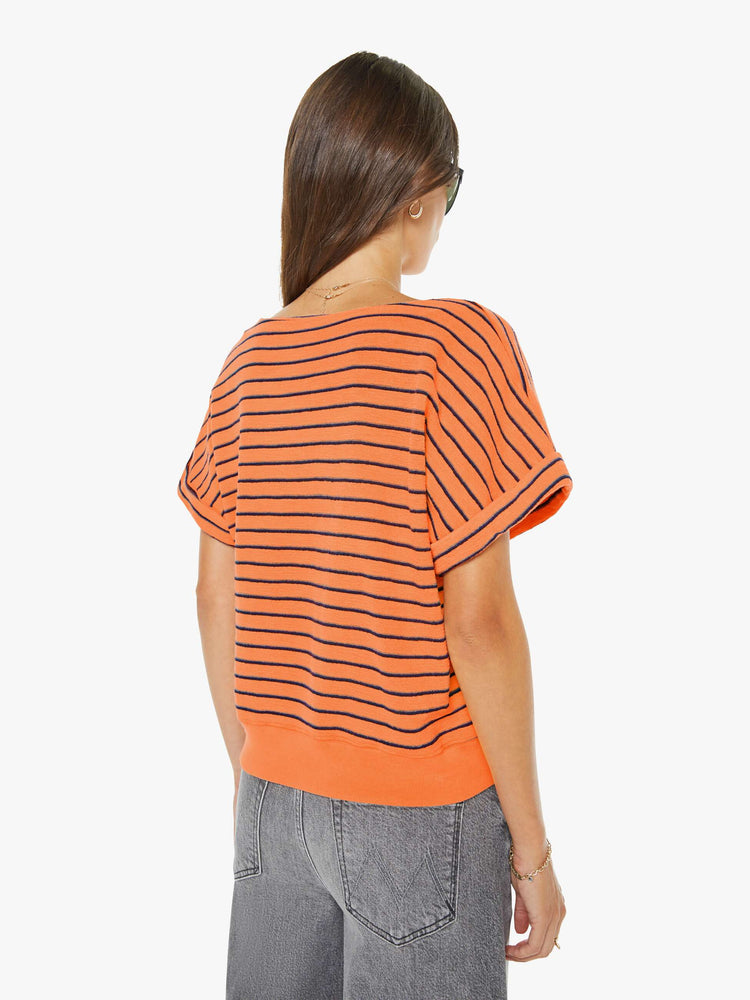 Back view of a woman in a bright orange and black stripes short sleeve tee with a boat neck and boxy fit.
