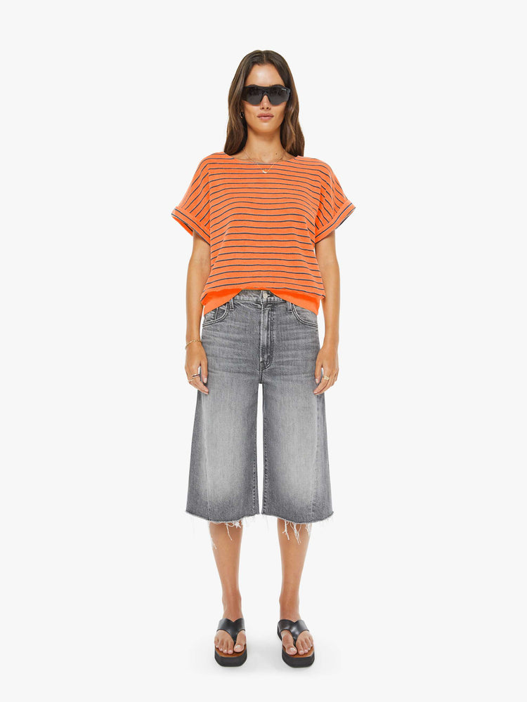 Front full body view of a woman in a bright orange and black stripes short sleeve tee with a boat neck and boxy fit.