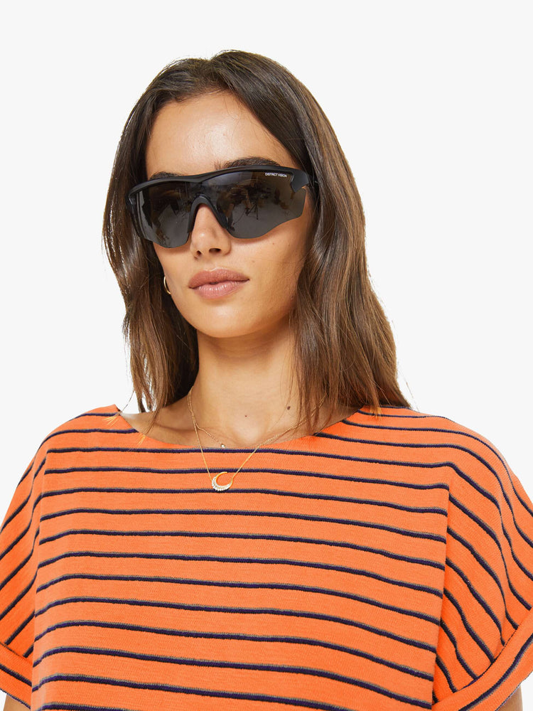 Front close up view of a woman in a bright orange and black stripes short sleeve tee with a boat neck and boxy fit.