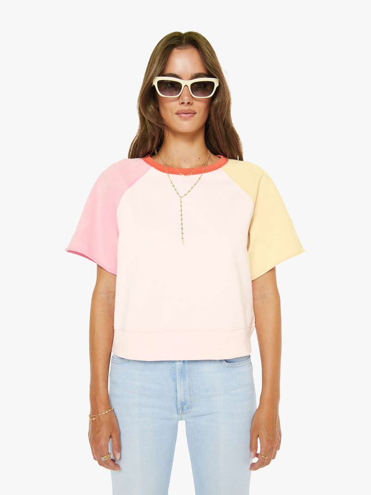 Front view of a woman in pale peach, baby pink and pastel yellow with orange trim at the neck crewneck sweatshirt with cut-off sleeves and a cropped, ribbed hem.