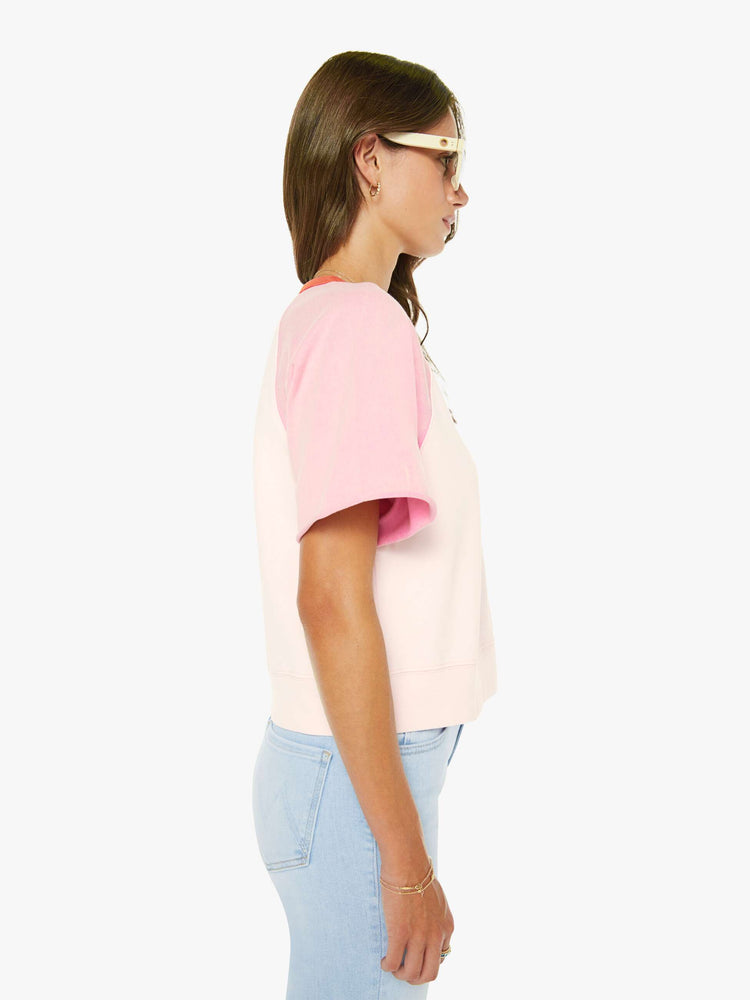 Side view of a woman in pale peach, baby pink and pastel yellow with orange trim at the neck crewneck sweatshirt with cut-off sleeves and a cropped, ribbed hem.