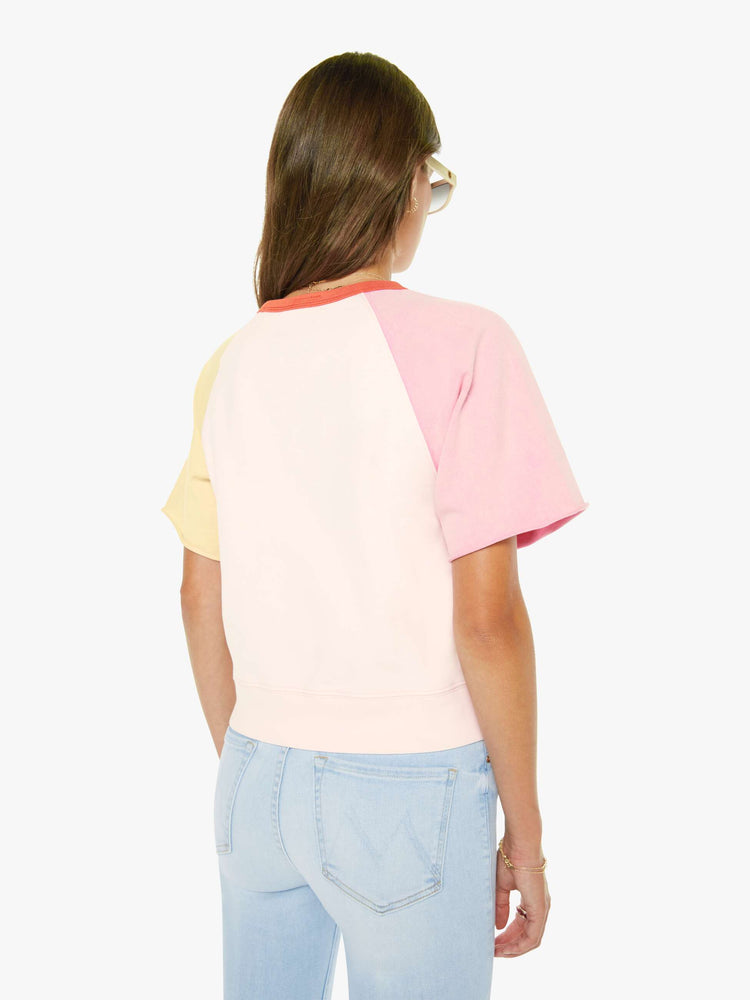 Back view of a woman in pale peach, baby pink and pastel yellow with orange trim at the neck crewneck sweatshirt with cut-off sleeves and a cropped, ribbed hem.