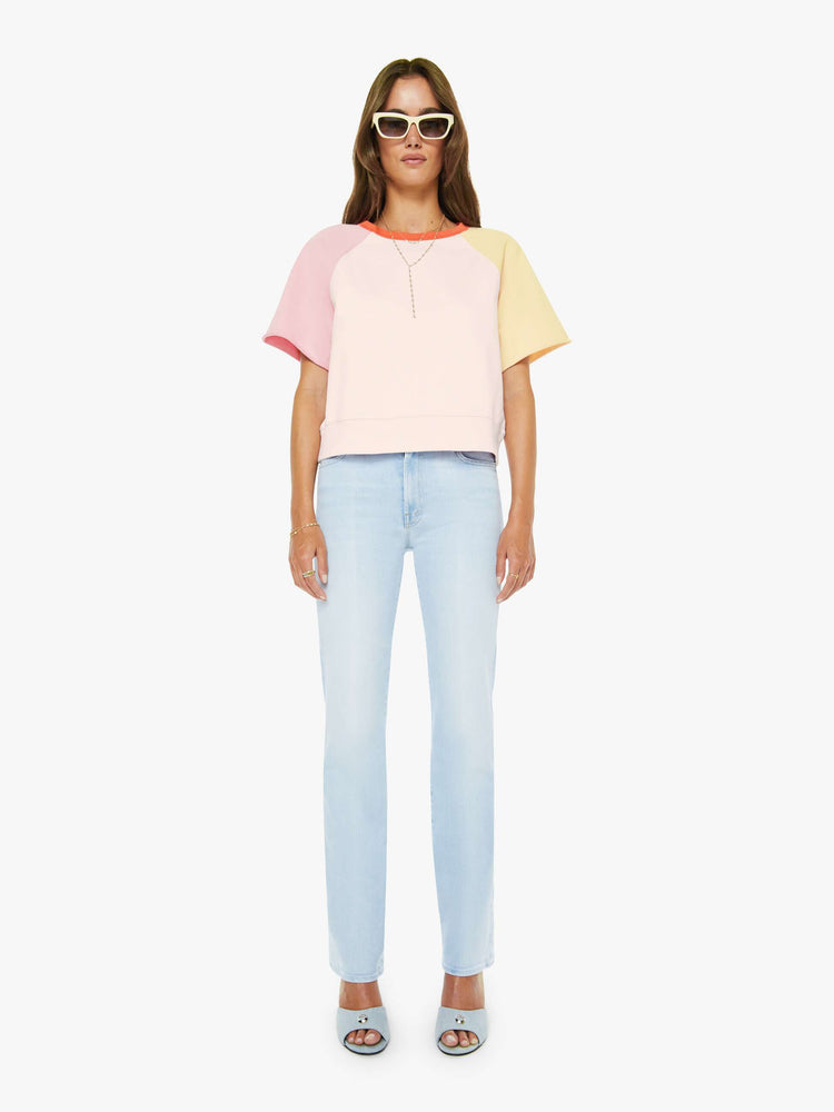 Full body view of a woman in pale peach, baby pink and pastel yellow with orange trim at the neck crewneck sweatshirt with cut-off sleeves and a cropped, ribbed hem.