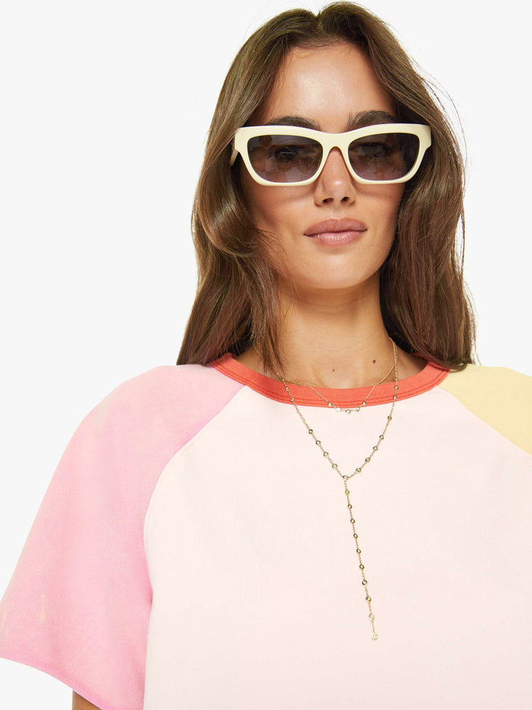 Close up view of a woman in pale peach, baby pink and pastel yellow with orange trim at the neck crewneck sweatshirt with cut-off sleeves and a cropped, ribbed hem.