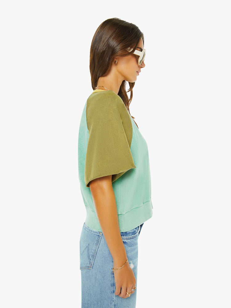 Side view of a woman in a cutoff sweater in a light blue and olive green with yellow trim at the neck.