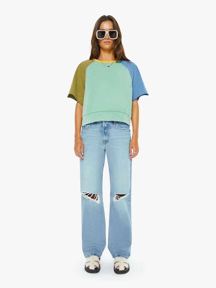 Full body view of a woman in a cutoff sweater in a light blue and olive green with yellow trim at the neck.