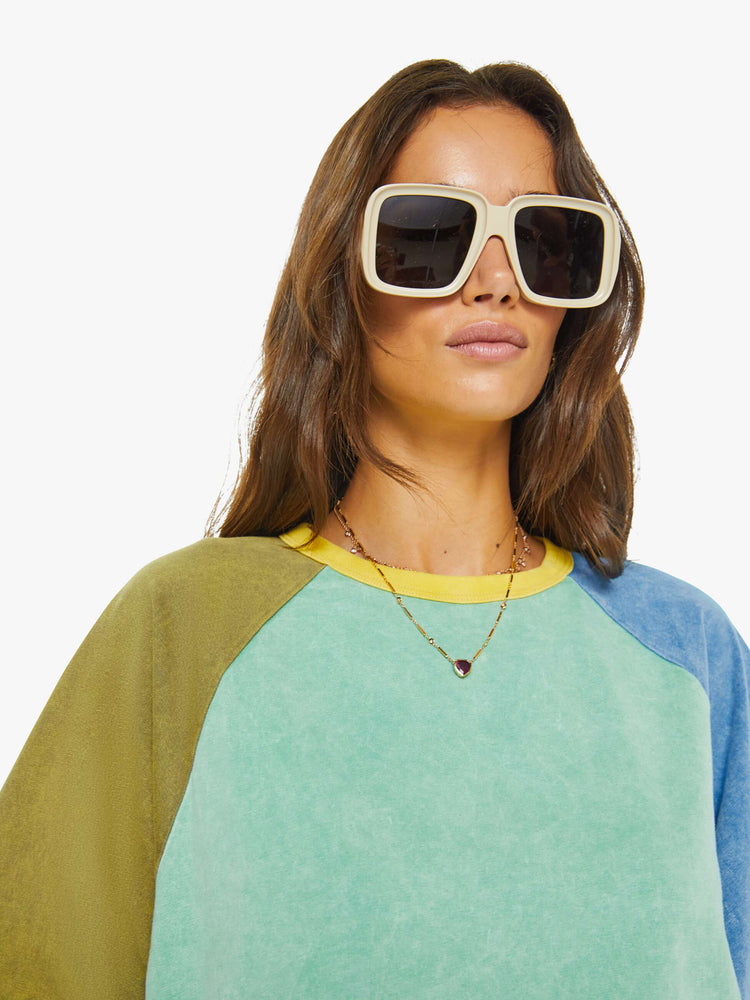 Close up view of a woman in a cutoff sweater in a light blue and olive green with yellow trim at the neck.