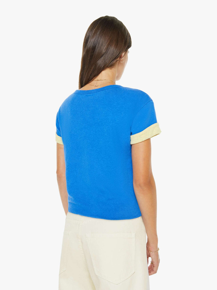 Back view of a womens blue tee in a cropped boxy fit featuring a white graphic and a yellow rolled cuff sleeve.