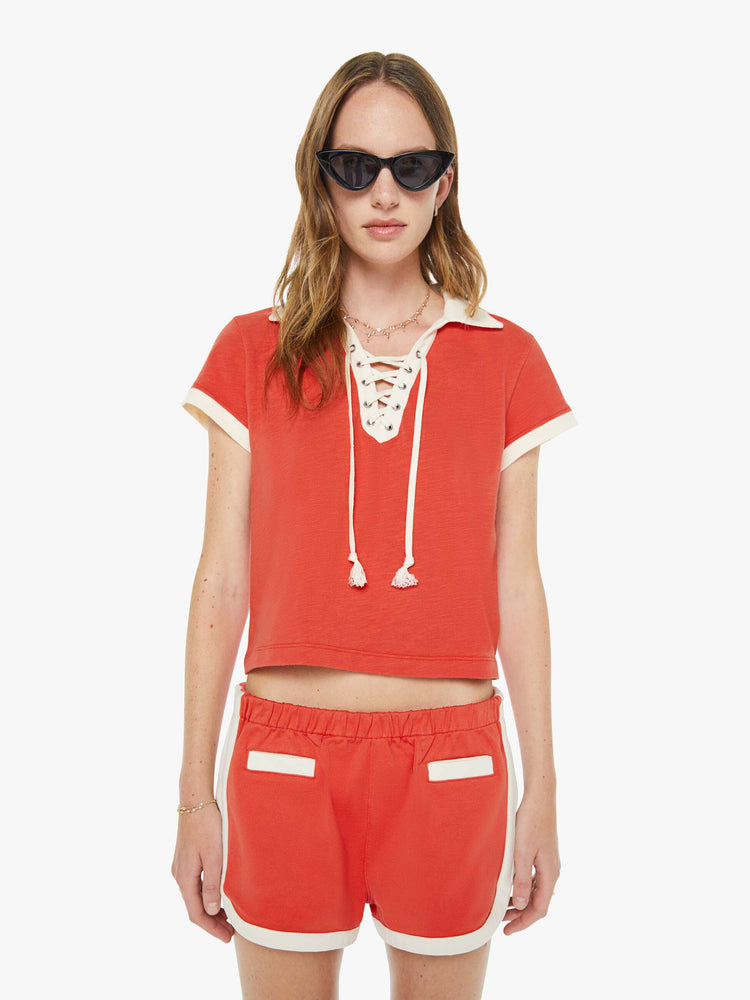 Front view of a woman in a fiery red collared tee with a V-neck that laces, short sleeves and a cropped, boxy fit.