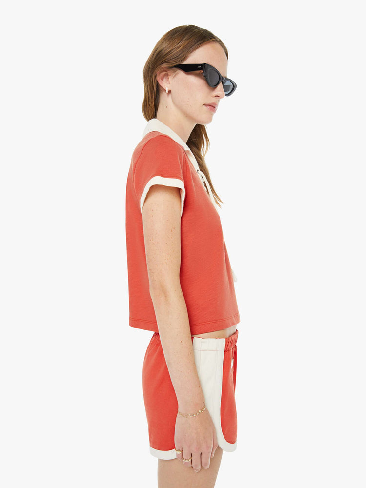 Side view of a woman in a fiery red collared tee with a V-neck that laces, short sleeves and a cropped, boxy fit.