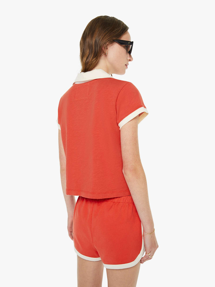 Back view of a woman in a fiery red collared tee with a V-neck that laces, short sleeves and a cropped, boxy fit.