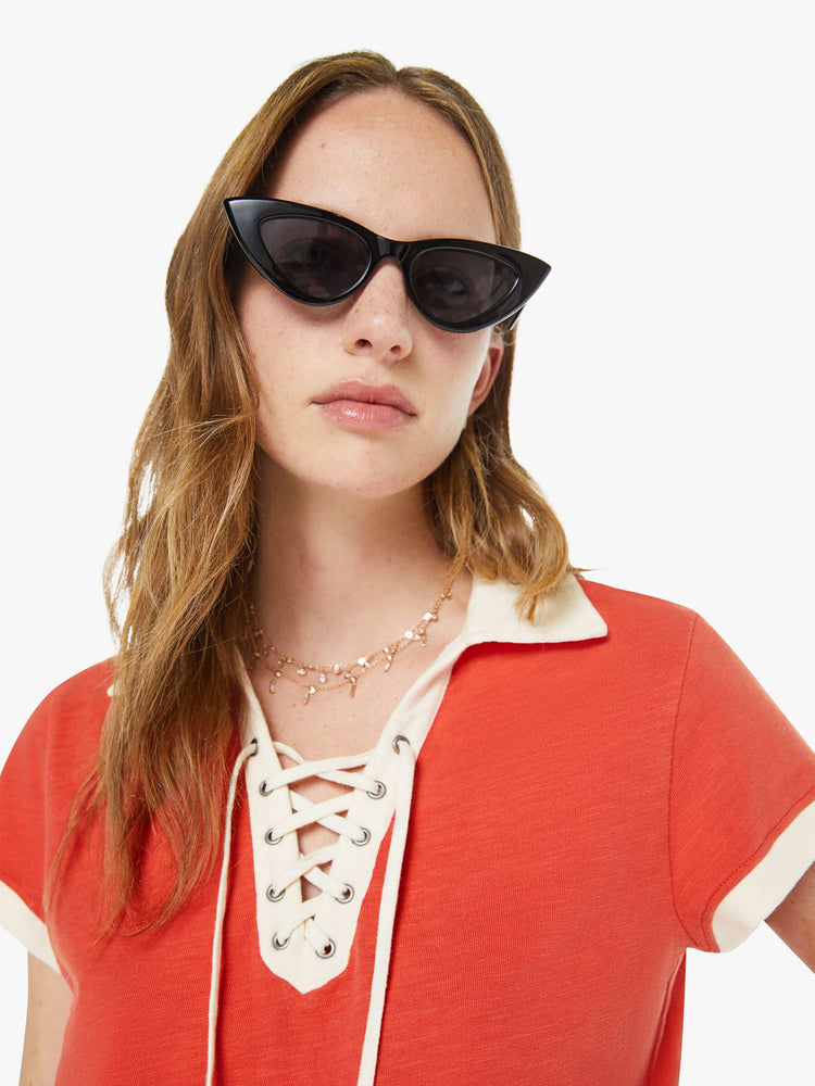 Close up view of a woman in a fiery red collared tee with a V-neck that laces, short sleeves and a cropped, boxy fit.