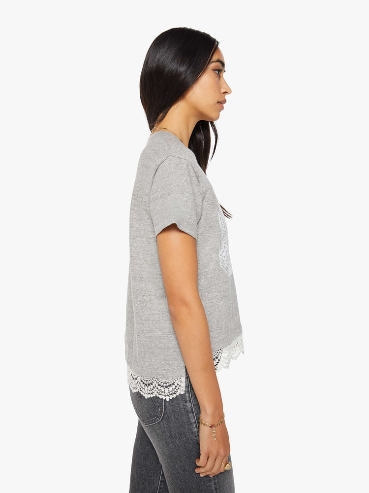 Side view of a woman in a heather grey with white lace applique on the front and lace trim oversized crewneck tee is designed with drop shoulders, short sleeves and a boxy fit.